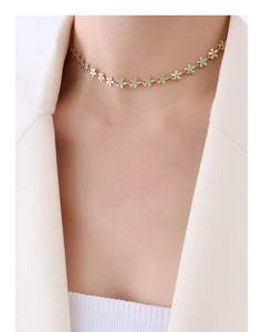 Detail of elegant gold flower necklace with blue enamel on a model in white blazer