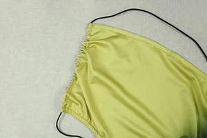 Detailed close-up of lime green ruched fabric and slim black straps on a mini dress