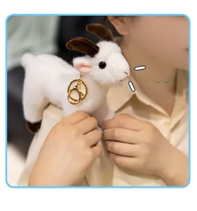 Cute white plush goat keychain accessory shown on a shoulder bag strap with gold clasp