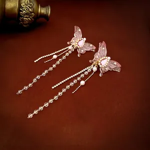 Pink butterfly tassel earrings with pearls and crystal accents on a dark leather background