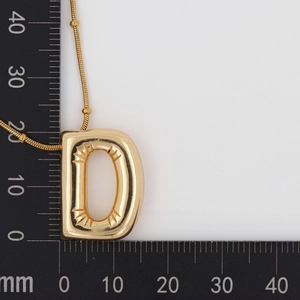 Detail view of gold letter D pendant showing 20mm by 25mm dimensions on a ruler