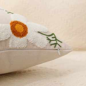 Macro detail of daisy floral embroidery and hidden zipper on beige tufted pillow cover