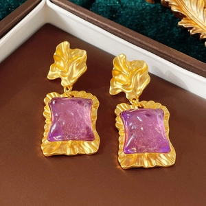 Détail macro de boucles d'oreilles fleur dorées avec pierres en résine violette