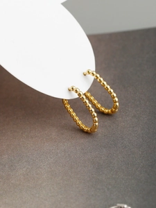 Close-up of gold beaded U-shape S925 sterling silver hoop earrings on a textured surface