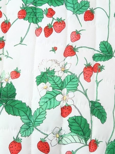 Close-up of quilted white fabric with red strawberry, green leaf and white flower patterns