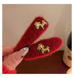 Dettaglio del fermaglio per capelli in peluche rosso con un cavallino a dondolo dorato