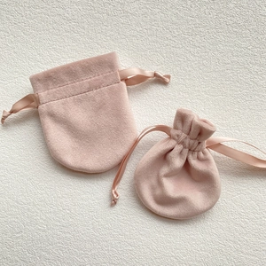 Pink velvet drawstring jewelry pouches in two sizes shown on beige textured background
