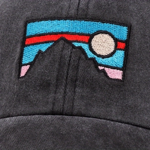 Close-up of grey baseball cap showing detailed embroidery with mountain and sky patterns