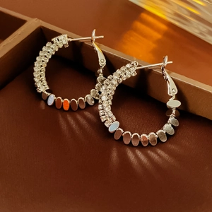 Macro shot of silver metal hoop earrings with sparkling zircon and colorful oval inlays