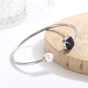 Dettaglio del bracciale rigido a C in argento con perla bianca e pietra blu su legno