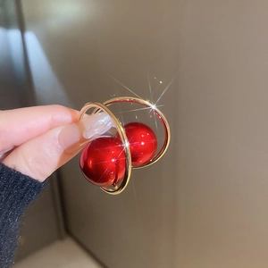 Detailed view of C-shaped gold earrings featuring a glossy red pearl with starburst glow
