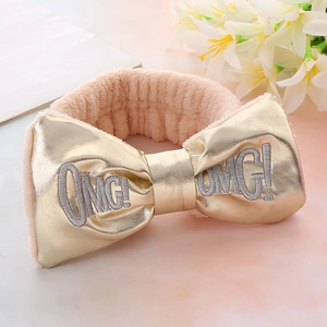 Detail of OMG! embroidered bow headband in metallic gold and soft beige plush fabric