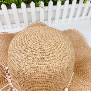 Detailed close-up of woven straw hat texture with wavy brim and wooden bead trim