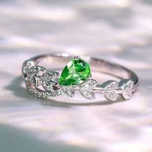 Vista macro de un anillo de hojas de plata con gema verde pera y diamantes pavimentados