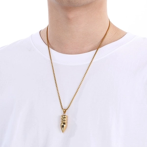 Detail of a gold bullet-shaped pendant on a chain worn by a male model on white background