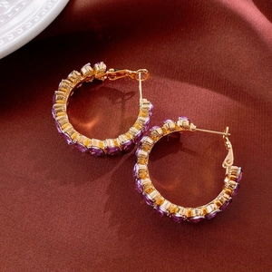 Macro shot of gold-plated hoop earrings with purple zircon stones on red satin background