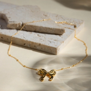 Close-up of a stylish 18k gold-plated bow necklace on elegant stone surfaces