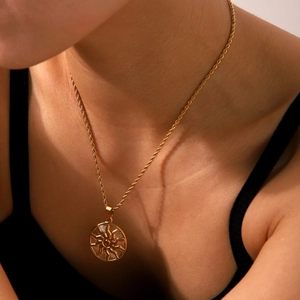 Close-up of golden sun totem pendant with twist chain worn on neck by a model
