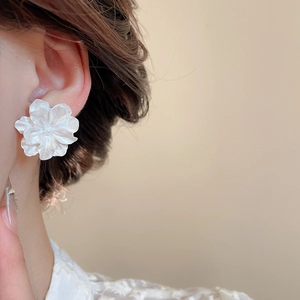 Dettaglio ravvicinato di un orecchino a fiore 3D bianco con petali perlescenti a strati