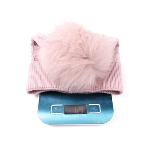 Bonnet en tricot rose avec pompon en fourrure sur balance affichant un poids de 129g