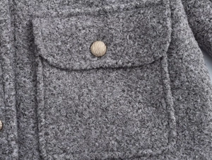 Vue macro détaillée du tissu sherpa gris avec un bouton en métal doré embossé et coutures