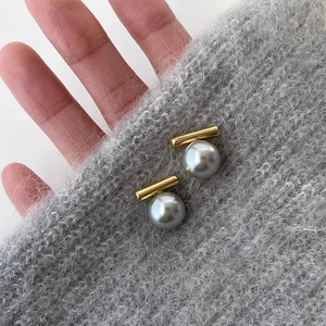 Nahaufnahme eleganter goldener Zylinderstäbe und großer grauer Perlenstecker auf Strick