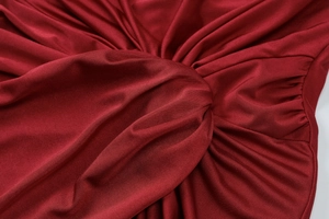 Detailed close-up of dark red gathered fabric with a stylish twist and premium knitted texture