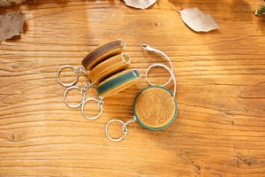 Detail of four handmade crazy horse leather mini tape measures on a rustic wood surface