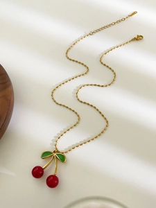 Detailaufnahme des roten Kirsch-Anhängers mit grünen Blättern an goldener Perlenkette