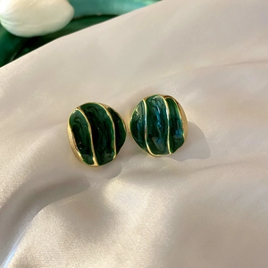 Macro shot of dark green enamel earrings with gold wavy texture on white silk fabric