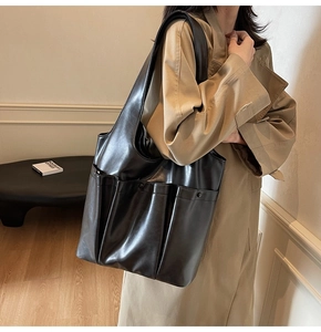 Close-up of black PU leather tote bag with multiple pockets worn over a beige trench coat