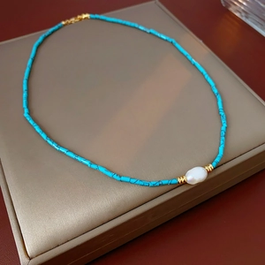 Detail of turquoise bead necklace featuring a central baroque pearl and golden spacers