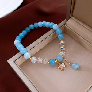 Detail of white crystal bracelet with blue beads and a gold cherry blossom pendant