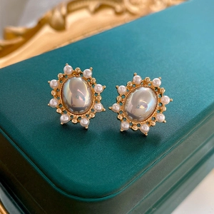 Macro detail of French vintage oval stud earrings with pearls on dark green jewelry box