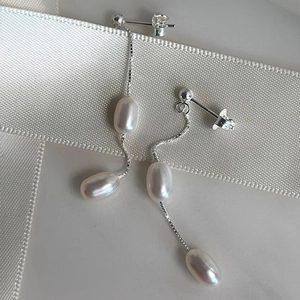 Detail of silver drop earrings with freshwater pearls on a white textured ribbon