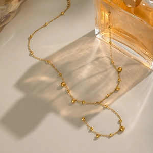 Detailed view of gold stainless steel Y-necklace featuring polished beads on a beige backdrop