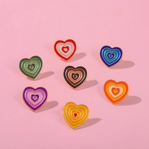 Detail of 7 heart-shaped enamel pins with colorful layered design on pink background