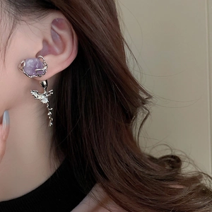 Close-up of liquid metal style silver earrings with a purple stone on a model's ear