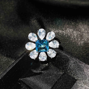 Macro shot of flower-shaped silver ring with square blue stone and pear-cut white gems