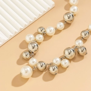 Detail of chunky faux pearl and polished silver bead necklace on elegant warm background