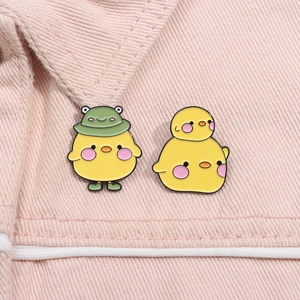 Close-up of cute enamel chick pins in frog costumes on pink denim fabric material