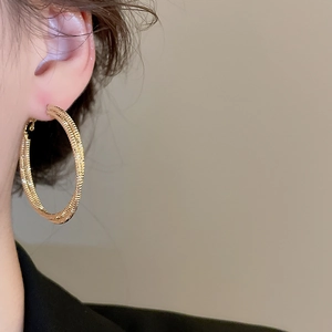 Detail of gold spiral hoop earrings with dual parallel twisted texture on a model