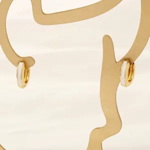 Detailed view of 18K gold plated hoop earrings with white enamel on an artistic stand