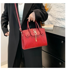 Model wearing a red crocodile embossed handbag with metal logo and tassel details