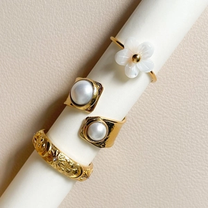 Gold stainless steel flower and pearl rings set displayed on white cylindrical pedestals