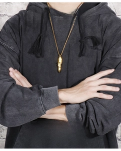 Detail of a men's gold bullet pendant necklace with intricate patterns on a grey hoodie