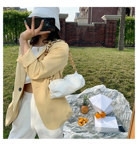 Chic white pleated dumpling bag with chunky gold chain strap held by a stylish model