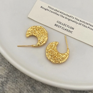 Gros plan détaillé de boucles d'oreilles dorées en C avec texture martelée sur céramique