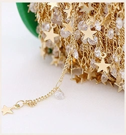 Macro shot of 14K gold plated chain with star pendants and clear crystals on a green spool