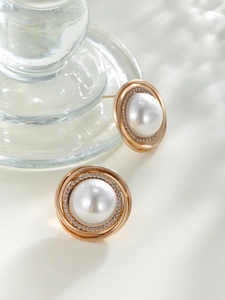 Macro detail of gold-plated stud earrings featuring a round pearl and sparkling zircon halo